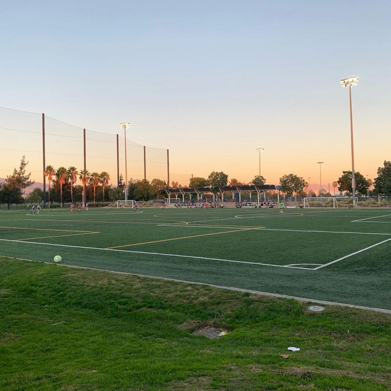 A soccer field is shown at sunset with multiple goalposts and surrounding nets, and there is a ball on the grass.