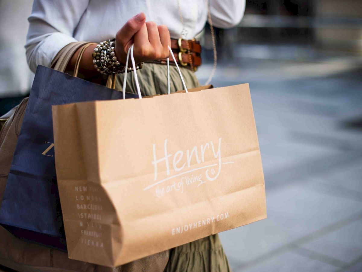 A person is holding shopping bags, with one brown paper bag labeled 