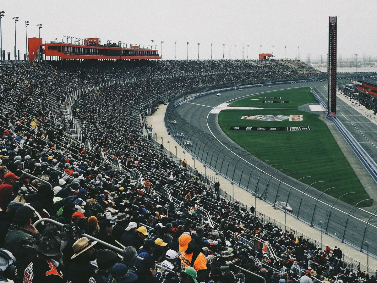 A crowded stadium with spectators watching an event at a racetrack, featuring an expansive view of the track and a large crowd in the stands.