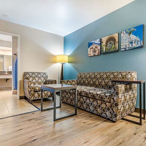 The image shows a modern living area with a sofa and chair, a coffee table, floor lamp, wooden flooring, and three pictures on the wall.