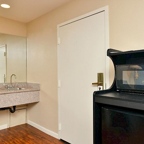 The image shows a motel or hotel room with a microwave and refrigerator unit, a sink with a mirror, and a door to the bathroom.