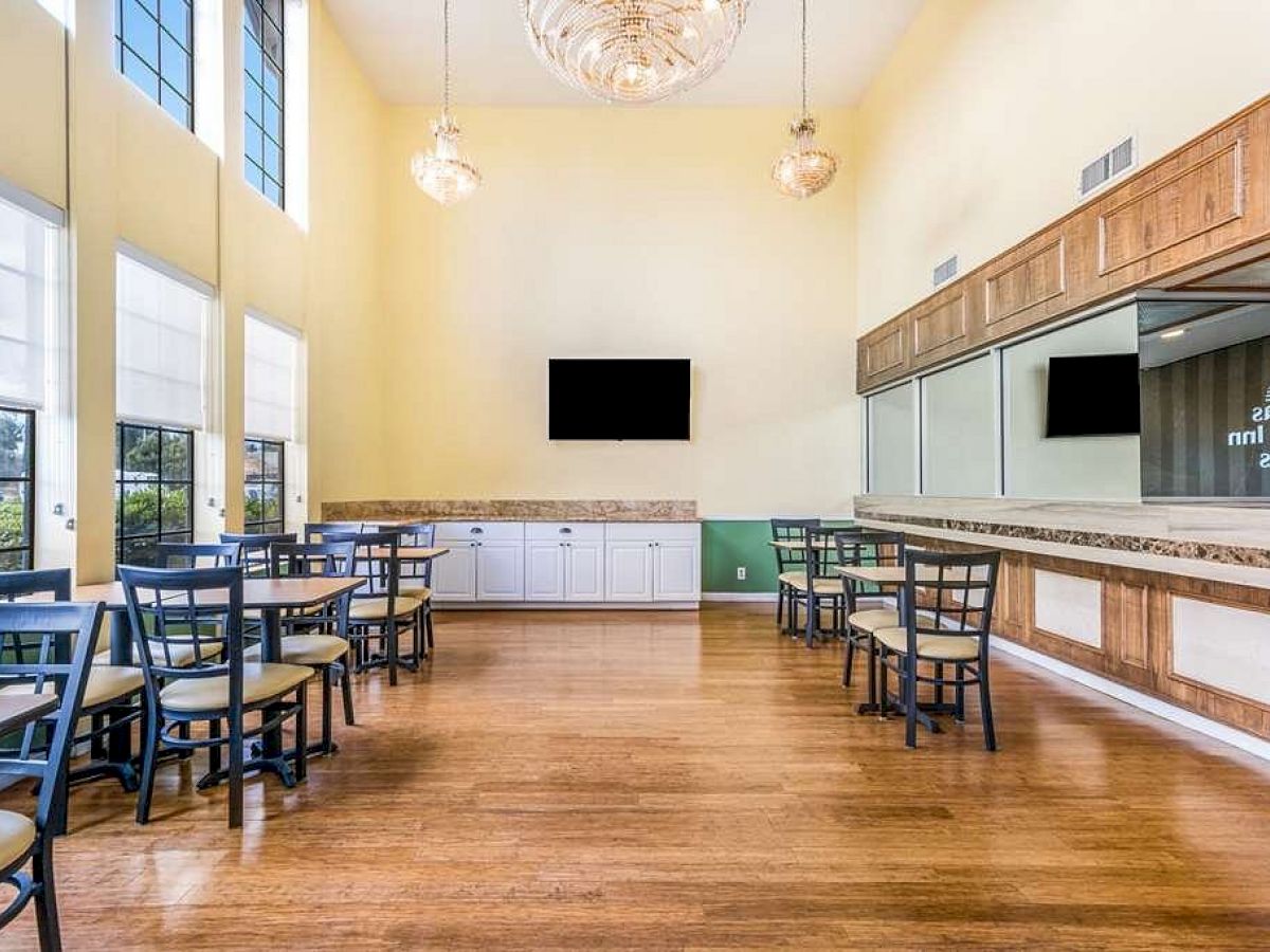 The image shows a bright dining area with several tables and chairs, a TV on the rear wall, and mirrors on the side.