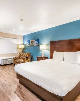 A hotel room with a large bed, two side tables, lamps, an armchair, a desk with chairs, and a TV on the wall, featuring blue accent walls.