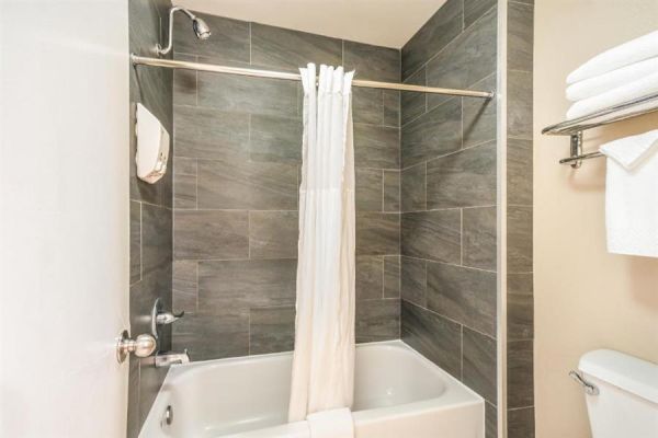 A bathroom with a tiled shower-tub combo, white curtain, and a towel rack holding folded towels and an additional towel hanging below it ends the sentence.