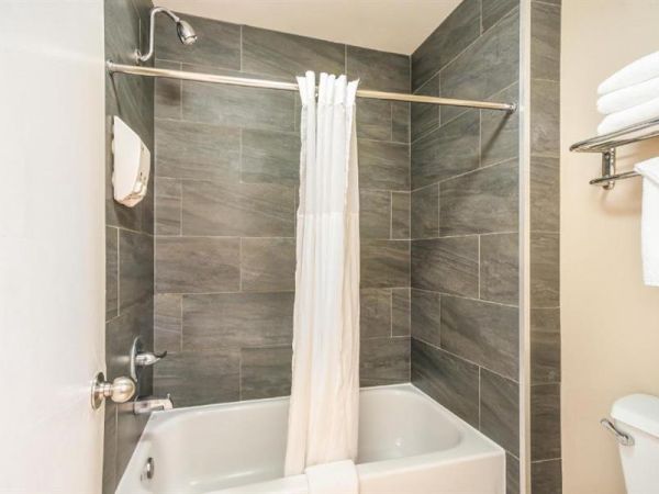 A bathroom with a tiled shower-tub combo, white curtain, and a towel rack holding folded towels and an additional towel hanging below it ends the sentence.