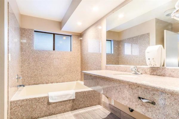 This image shows a clean, modern bathroom with a bathtub, a large countertop with a sink, and a mirror above. The walls are tiled, and lighting is ample.