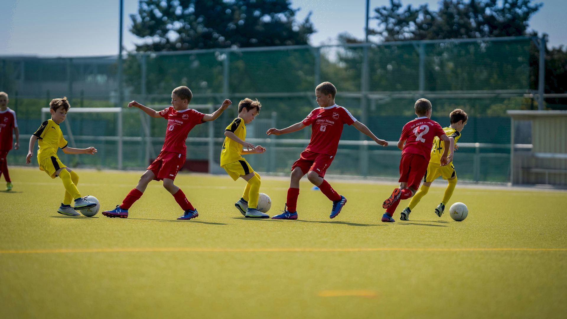 Children playing soccer on a field, wearing red and yellow uniforms, actively chasing the ball in a game.