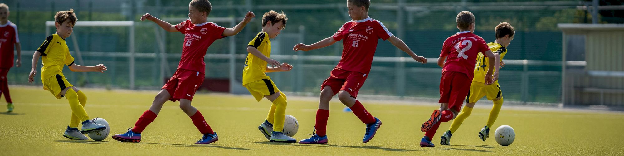 Children playing soccer on a field, wearing red and yellow uniforms, actively chasing the ball in a game.