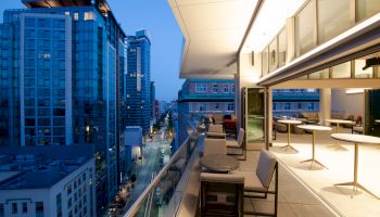 A modern balcony with seating, overlooking a city street lined with high-rise buildings during twilight.