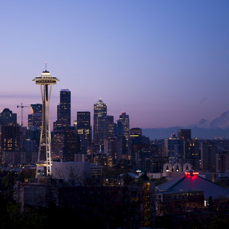 This image features the Seattle skyline at dusk, with the Space Needle prominently in the foreground and Mount Rainier visible in the background.