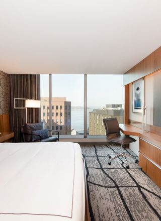 A modern hotel room featuring a large bed, wall-mounted TV, desk with chair, cityscape view from the window, and stylish decor finishes the sentence.