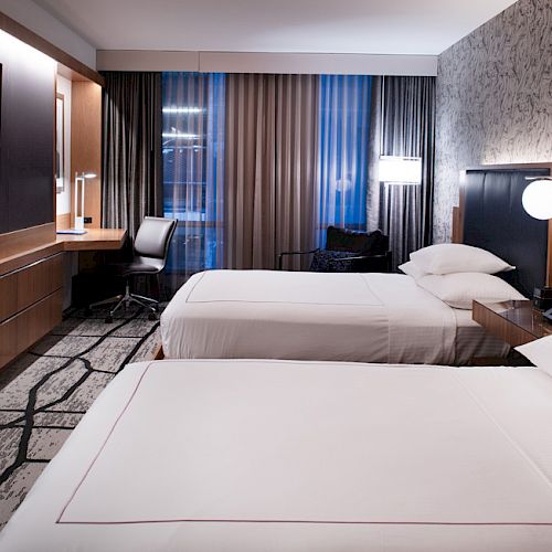 A modern hotel room with two double beds, a flat-screen TV, a desk, and contemporary decor. The atmosphere is clean and welcoming.