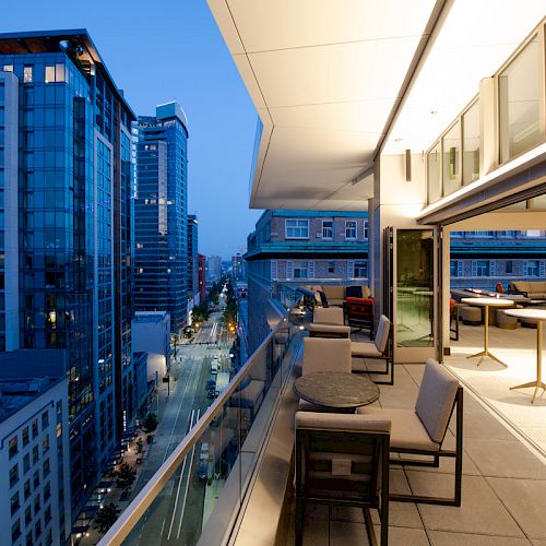 A modern cityscape with tall buildings at dusk, and a luxurious terrace featuring tables, chairs, and open space for relaxation or gatherings.