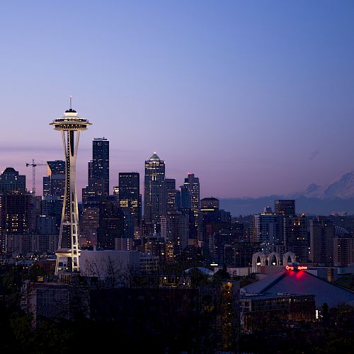 The image shows the Seattle skyline at dusk, including the Space Needle and various buildings, with Mount Rainier visible in the background.