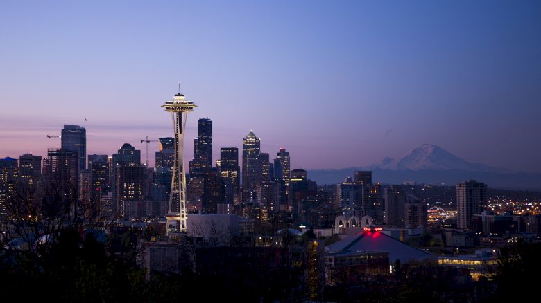 The image shows the Seattle skyline at dusk with the Space Needle prominently lit, and Mount Rainier visible in the distance.