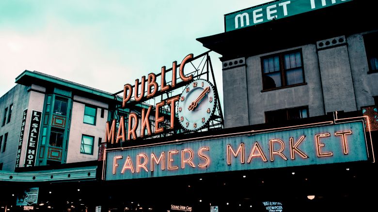 This image shows a neon sign for "Public Market" and "Farmers Market" on a building facade, with a clock in between the words.