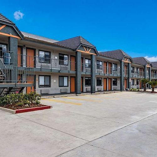 A two-story motel with exterior corridors, parking lot, staircases, and blue sky with clouds in the background.