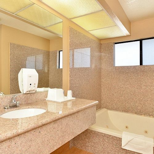 The image shows a bathroom with a marble countertop, sink, soap dispenser, and cups, along with a bathtub and a large mirror.