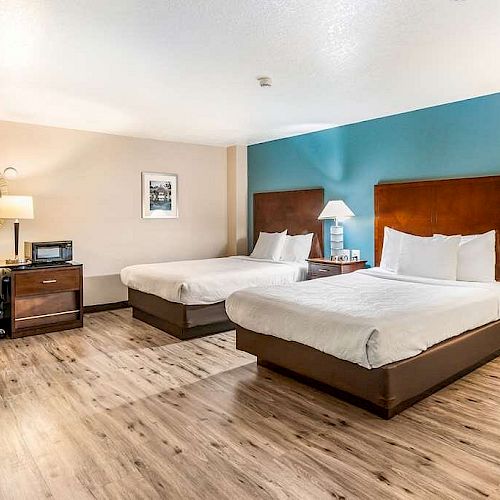 A hotel room with two beds, a desk, TV, microwave, and a round mirror on a beige and blue accent wall.