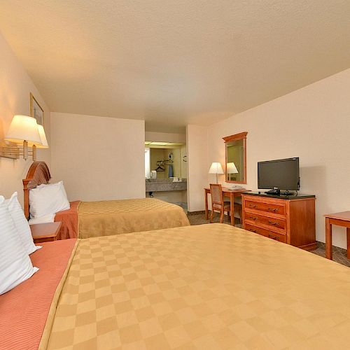 A hotel room with two beds, a TV on a dresser, a mirror, and a small vanity area in the background, decorated in warm tones.